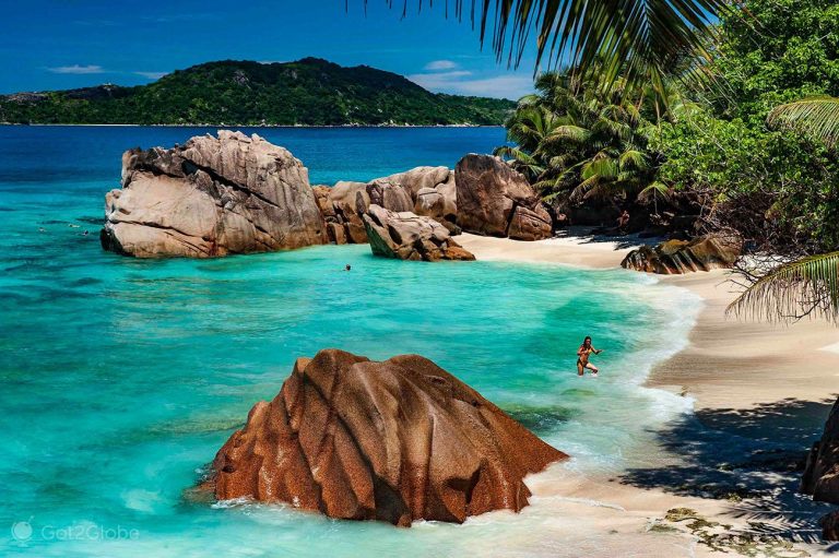 Plage de sable blanc aux Seychelles avec rochers et végétation luxuriante