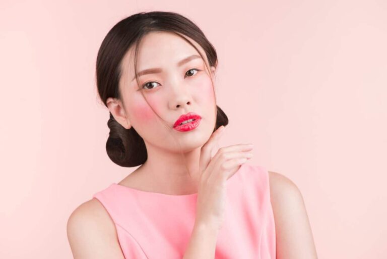 Jeune femme asiatique avec un maquillage professionnel et une coiffure élégante sur fond rose