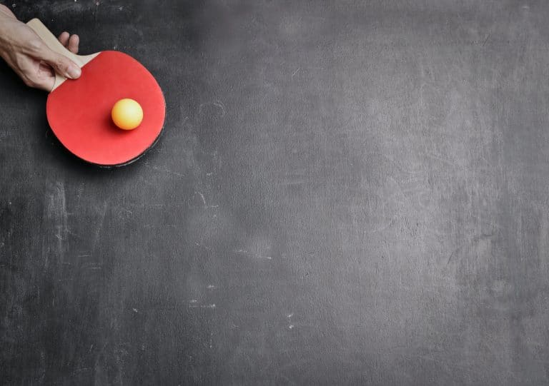 Main tenant une raquette et une balle sur une table de ping-pong