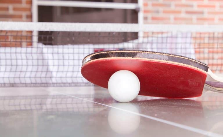 Balle de ping-pong sous une raquette rouge sur une table